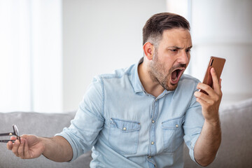 Portrait of angry young man screaming on his mobile phone. Portrait of a furious young businessman yelling at mobile phone. Aggressive man in blue shirt screaming at smartphone