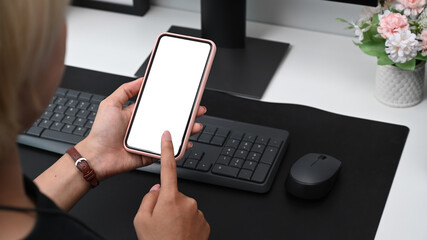 Close up over shoulder view of young woman sitting at her workplace and using mobile phone.