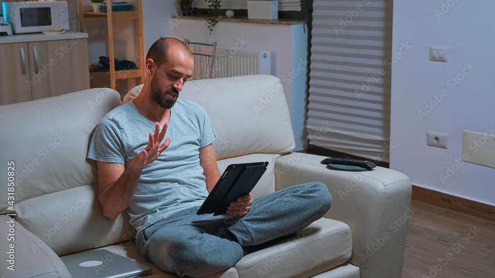 Poster focused man with beard sitting on couch in front of television while talking with teammates during o