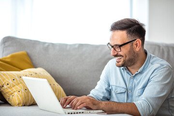 Happy young businessman using laptop at home. Young man working on computer at home. Casual entrepreneur feeling excited about new project while working on laptop at home.