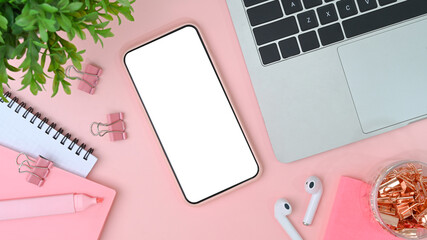 Female workspace with mobile phone, laptop, earphone, notebook and plant on pink pastel background.