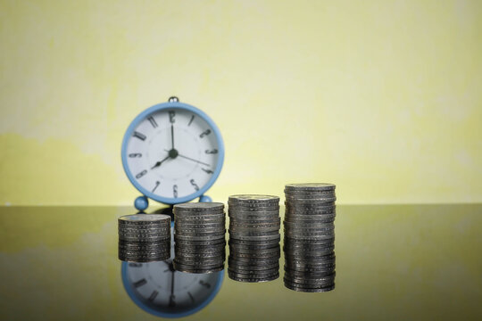 Stacked coins with an alarm clock at the back creating a blur effect.  Time and business concept