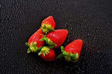 Red and ripe strawberries with green leaves on a black background and water droplets symbol of freshness