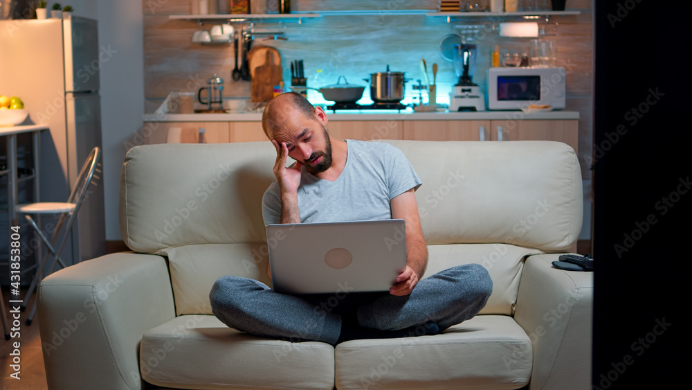 Poster tired man in pajams browsing on internet lifestyle information using laptop computer sitting on sofa