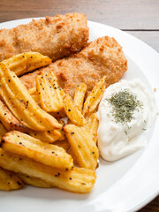 Traditional fish and chips dish with white mayo sauce and dill herbs on white plate. Common take away meal in English speaking nations. Cooked cod with peppered potato fries. Selective focus.