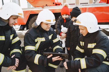 Male firefighters show children on a tablet safety rules