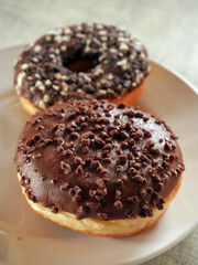 Doughnut with chocolate icing on a white plate. Pastry product. Delicious and unhealthy choice of desert