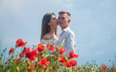 Happy couple in love kissing in beautiful field of poppy flower on romantic day, love