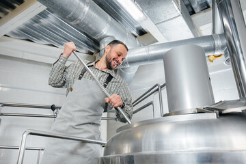 A young male brewer is engaged in the brewing process in a small brewery. Beer production.
