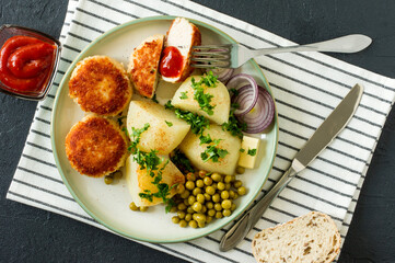 Top view of chicken breaded roasted cutlets with boiled potato and germinated green pea served with onion and ketchup.