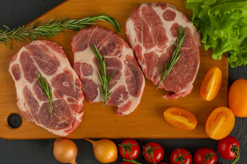 Raw pork steakes - ready for cooking with herbs and tomatoes. wooden background