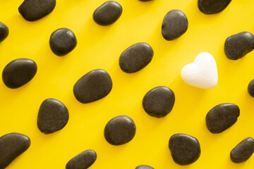 black stone with one white heart on yellow backgorund.flat lay pattern concept