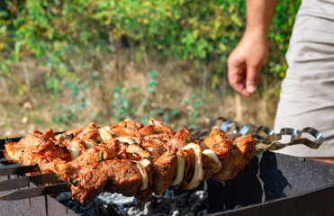 Man cooking meat on metal skewers. Barbecue outdoors. Weekend picnic.