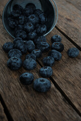 Blueberry berries spilled from metal bucket onto wooden table.