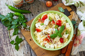 Food dieting concept, tabbouleh salad. Couscous salad with feta cheese, tomatoes, basil and chili on a rustic wooden table.