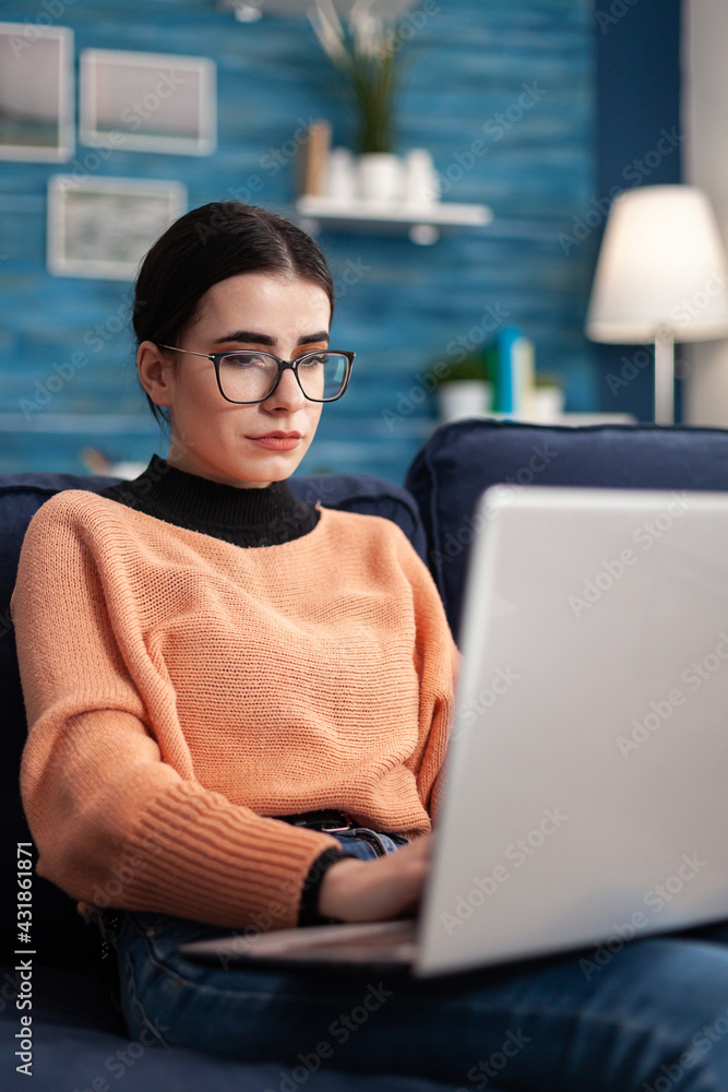 Poster student browsing online commerce information using laptop computer while sitting comfortable on sofa