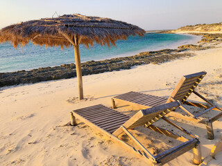 [Madagascar] Two wood benches and a palm leaf umbrella on a white sand beach in Andavadoaka