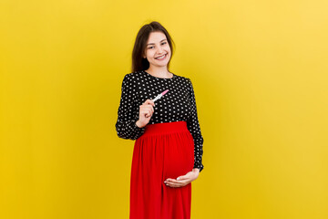 positive pregnancy test with two stripes against happy pregnant woman abdomen at Colored background. Future mother in gray dress. Pregnancy surprise. Copy space