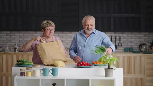 Elderly People Are Unpacking Food After Shopping In Grocery Or Market, Taking Fresh Vegetables From Eco Paper Bag