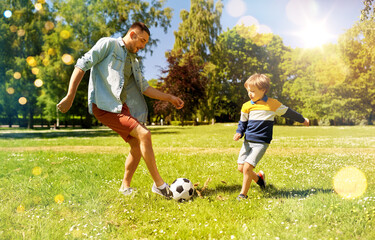family, fatherhood and people concept - happy father and little son with ball playing soccer at summer park