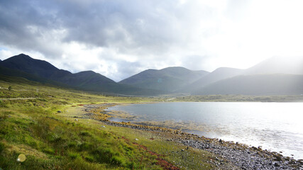 Fototapeta na wymiar Loch Ainort und Loch na Cairidh auf der Insel Skye mit malerischem gleißendem Sonnenlicht, Bergen und spiegelung im Ufer