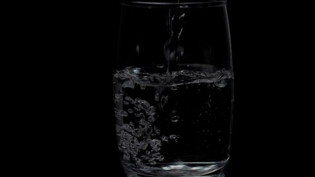 More water is added / pouring to an already filled glass of water - hygienic drink . Closeup shot of round bubbles rotating inside a sparkling glass of water kept against a black background
