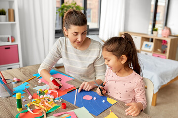 family, art and craft concept - mother spending time with her little daughter with glue making applique of color paper at home