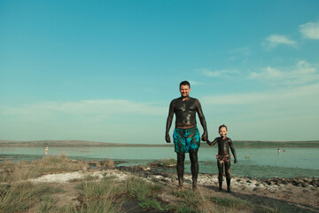 therapeutic mud for the body. mud baths on the lake. a man and a child are smeared with clay....