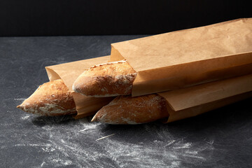food, baking and cooking concept - close up of baguette bread in paper bags on table over dark...