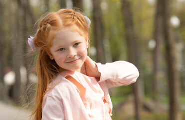 Little beautiful red hair girl smiling happily in summer in the park.