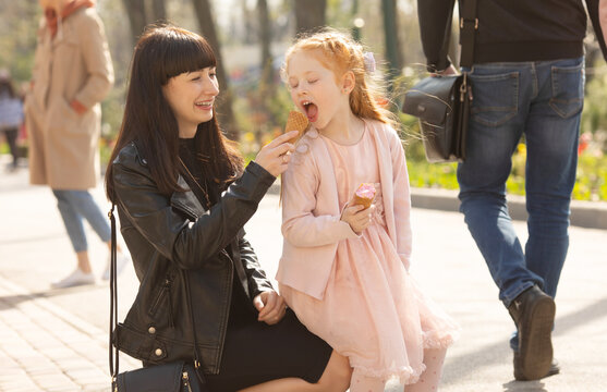 Mom and daughter eating ice cream in a park. Mother and red hair child have fun. Relaxing family time.