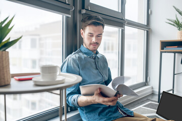 Young businessman scrutinizing project documentation and looking involved