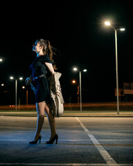 Girl in a coat in the parking lot against the backdrop of the night city with lanterns