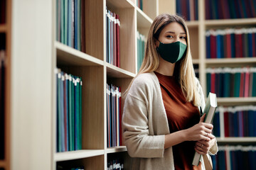 Portrait of happy student with face mask at college library.