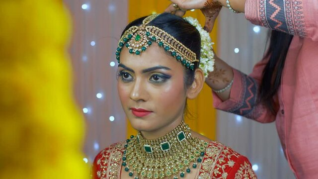 Indian bride getting ready - Putting Gajra or floral garland on a bride's hair bun. North Indian bride with green-gold heavy jewelry and Beli flower Gajra - Indian wedding / matrimonial day
