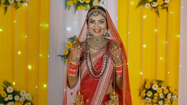 Pretty Indian bride holding her Ghoonghat/veil posing in her marriage ceremony. Medium shot of a lovely girl in her traditional wedding dress with Chuda and Kalire blushing with happiness - Hindu m...