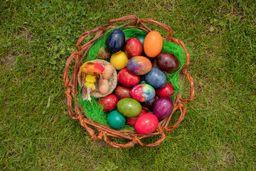 Basket with painted, coloured Easter eggs, flat lay on the grass.