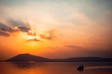 A beautiful golden sunset on the lake. Locals ride in a boat on a lake during a beautiful sunset. Sunset or sunrise landscape, panorama of beautiful nature.