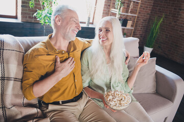 Photo of old impressed funny grandmother grandfather sitting sofa laughing eating pop corn watching...