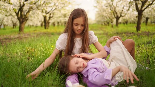 two long-haired girls sisters on the lawn in the garden with flowering trees.