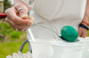 The hand holds a spoon and pulls out a green egg from Easter paints - Powered by Adobe