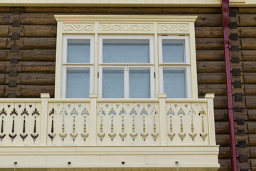 Wooden wall of an old house made of logs. Three-section window with light frames. Balcony in vintage style.