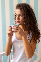 Beautiful cheerful young woman holding coffee cup and looking away at home