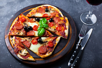Homemade italian pizza with mozzarella, pepperoni sausages, olives and basil and a glass of red wine on the table