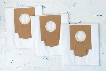 Three new empty dust bags for the vacuum cleaner are lying on white with blue spots wooden boards