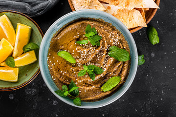  Traditional oriental appetizer baba ganoush with sesame seeds and mint leaves close-up. Eggplant hummus with pita crisps