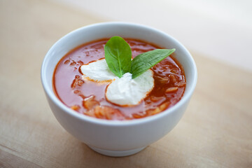 Hearty Italian minestrone vegetable soup made with tomato broth with sour cream decorated with basil leaves