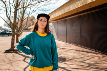 A portrait of young Caucasian hipster woman poses with a skateboard. In the background, an alley. Concept of sports lifestyle and street culture