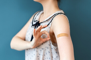 The covid-19 vaccine. A woman in a blouse shows her hand with a band-aid and makes an OK gesture. Dark blue background. The concept of immunization and vaccination against coronavirus
