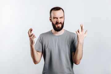 Handsome young man frown and cross fingers in hope on white background with space for advertising mock up